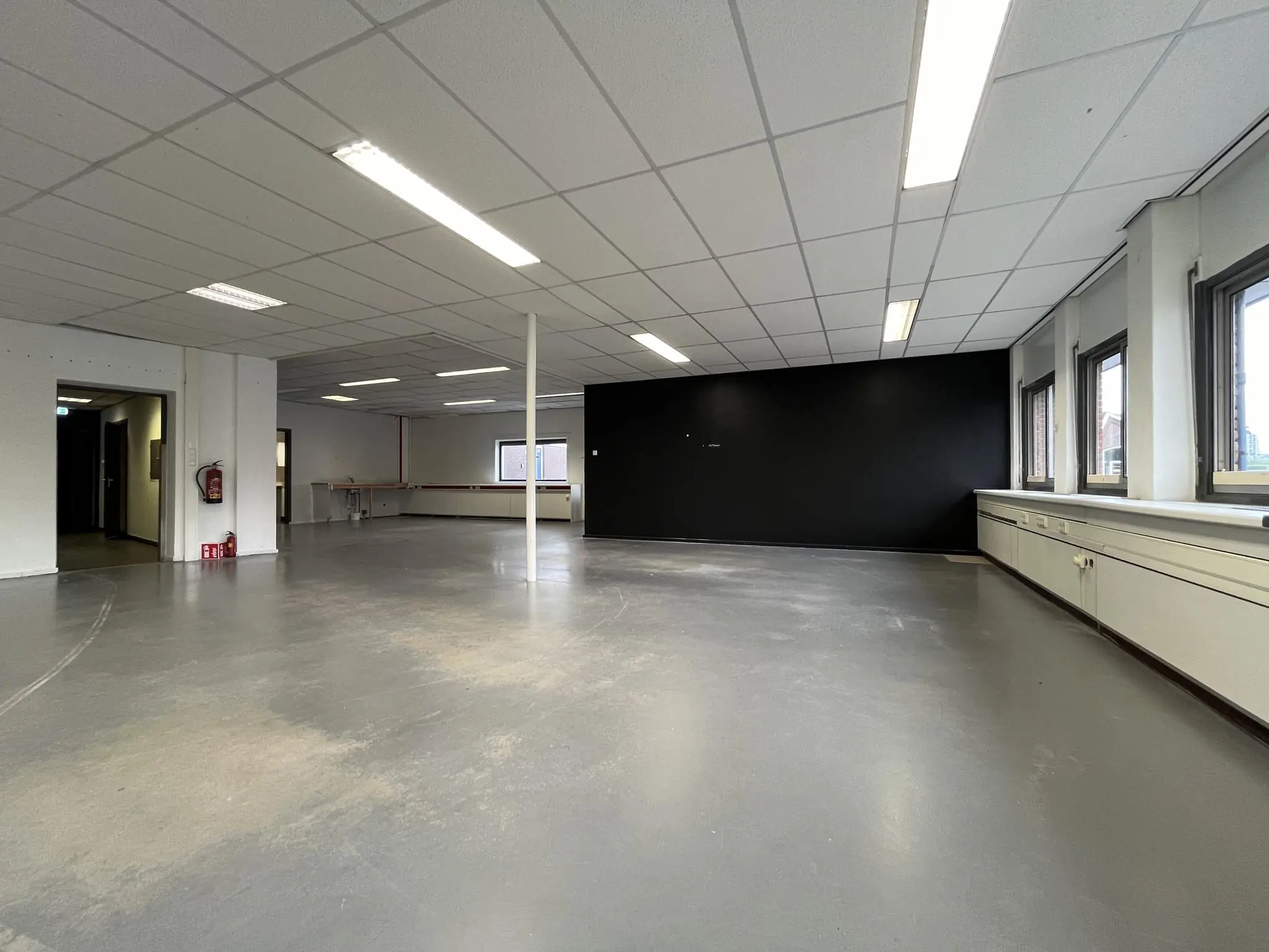 Lege kantoorruimte aan de 2e Daalsedijk met grijze vloer, systeemplafond en zwarte accentmuur.